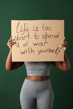 Woman holding a placard with motivational message against green background.