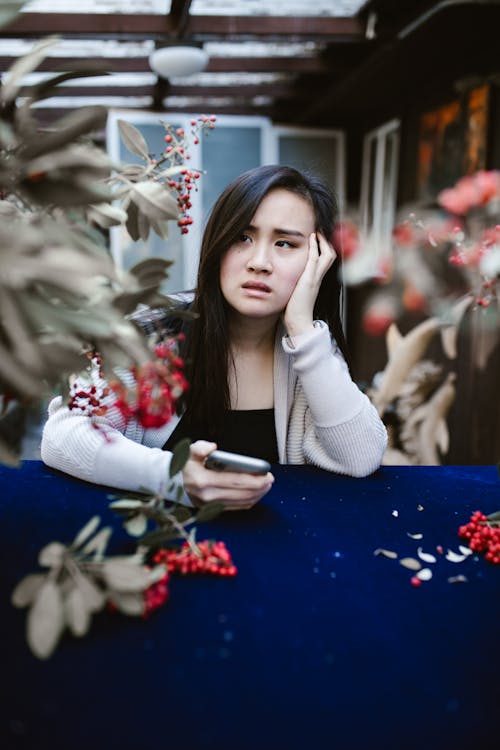 Free Sad Woman Looking Away While Holding her Smartphone Stock Photo