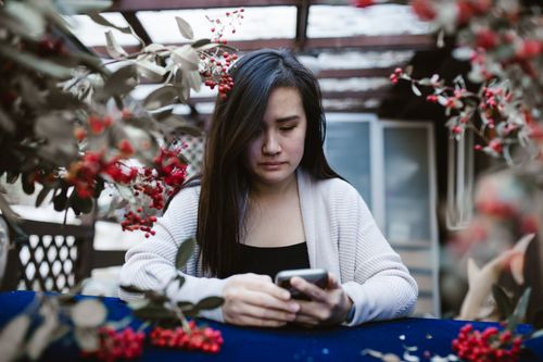 Free A contemplative woman using her smartphone outdoors surrounded by foliage. Stock Photo