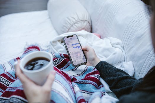 Person relaxing indoors with coffee and smartphone, texting in a cozy setting.