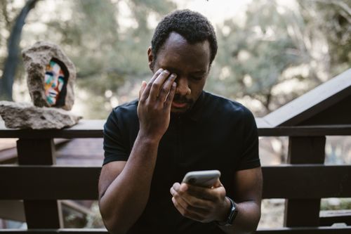 Free A man stands on a balcony outdoors, holding a smartphone, deep in thought. Stock Photo