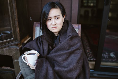 Free Woman Sitting Wrapped in Blanket with a Coffee Mug Stock Photo