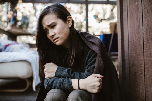 Free An Asian woman sits thoughtfully, wrapped in a blanket, in an indoor setting, conveying deep emotions. Stock Photo