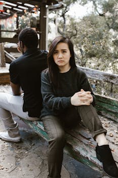 A couple sits back-to-back on a bench, expressing tension and conflict.