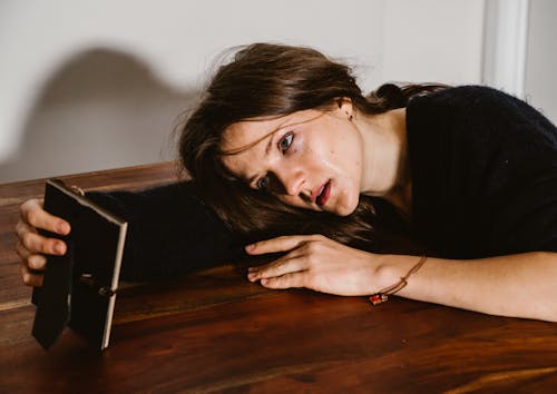 A Woman in Black Top Holding a Picture at a Wooden Table