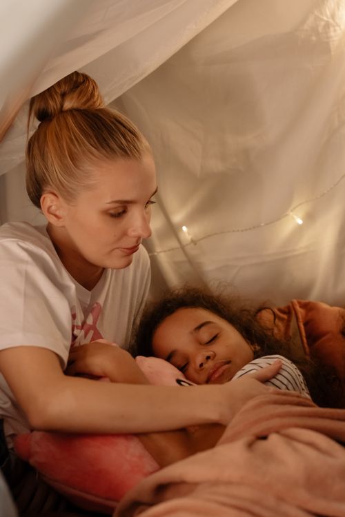 Free Heartwarming scene of a mother embracing her sleeping daughter in a cozy indoor setting. Stock Photo