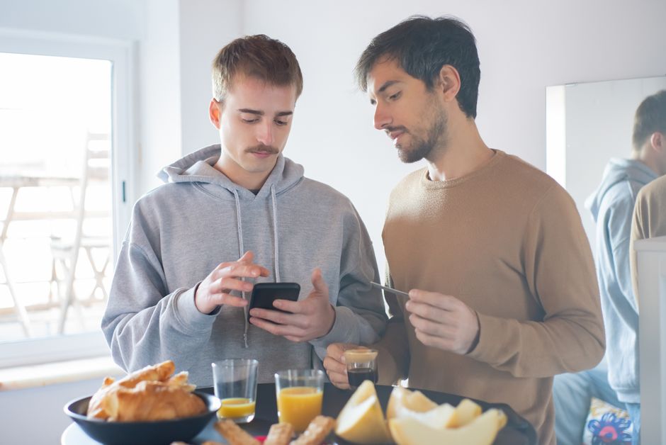 Two young men enjoy a breakfast in Portugal using a smartphone indoors, highlighting a relaxed lifestyle. Two young men enjoy a breakfast in Portugal using a smartphone indoors, highlighting a relaxed lifestyle.