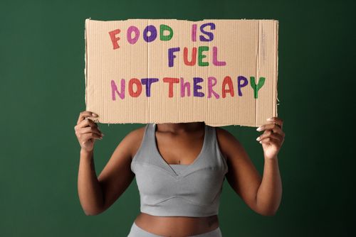 Free A woman holds a sign saying 'Food Is Fuel Not Therapy' against a green background. Stock Photo
