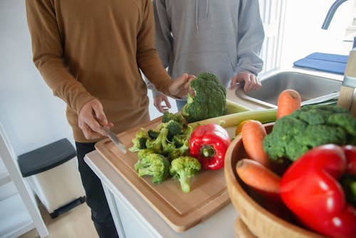 A Person in Brown Sweater Slicing the Broccoli on Wooden Chopping Board