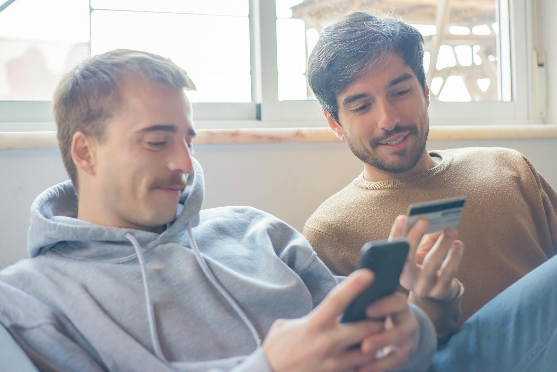 A smiling couple relaxing indoors shopping online with a smartphone and credit card.