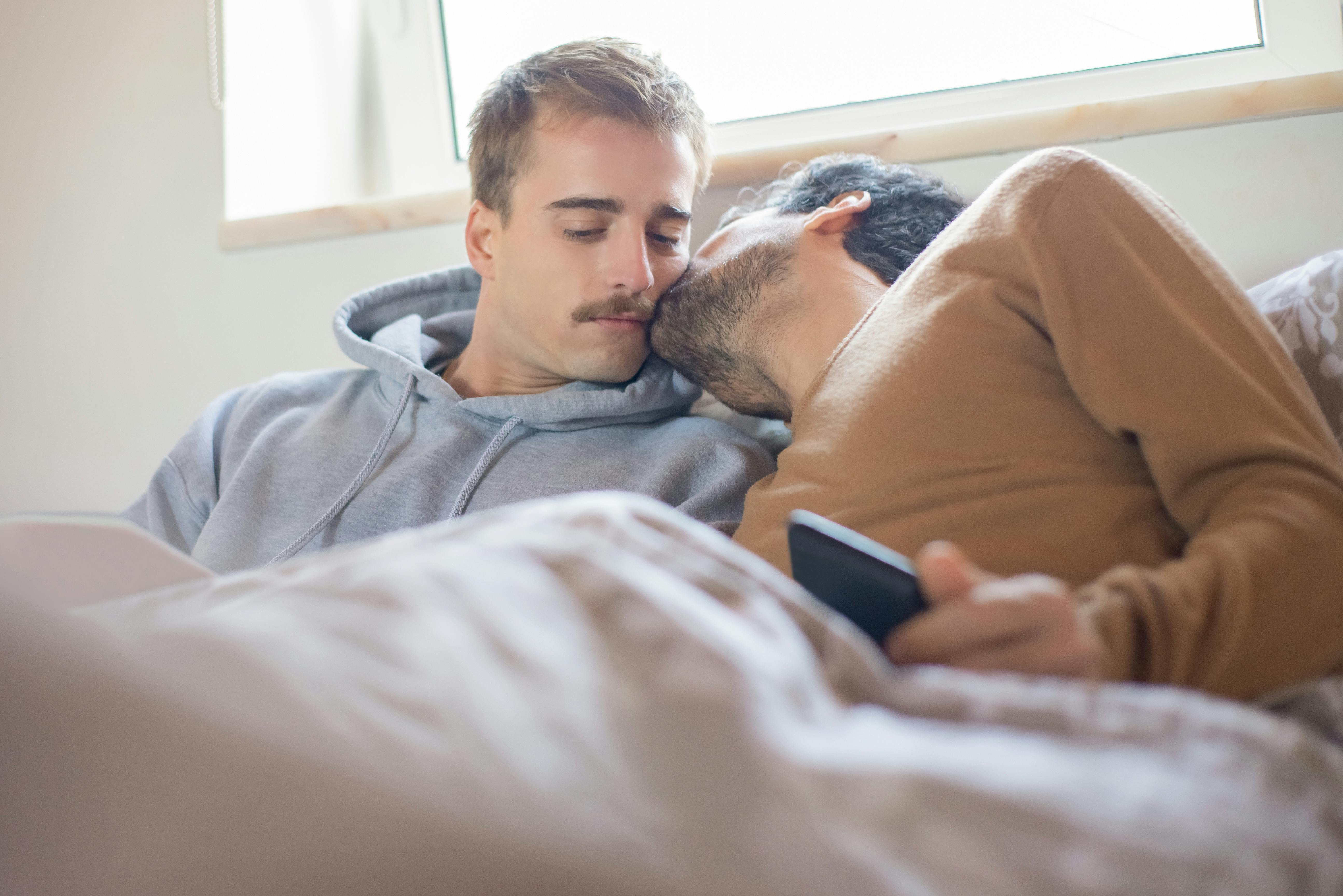 a man in a brown shirt kissing a man in a gray hoodie