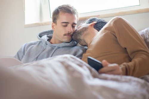 Free A Man in a Brown Shirt Kissing a Man in a Gray Hoodie Stock Photo