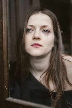 Portrait of a woman looking thoughtful and sad through a glass window. Emotional and poignant.