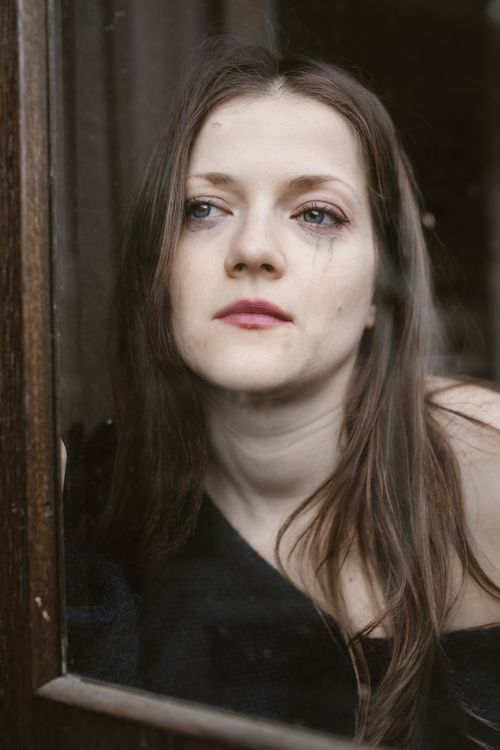 Free Portrait of a woman looking thoughtful and sad through a glass window. Emotional and poignant. Stock Photo