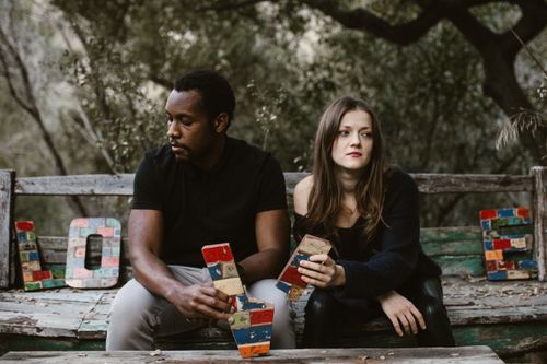 Free A couple sits in tension on a bench surrounded by nature, holding colorful blocks spelling 'Love'. Stock Photo