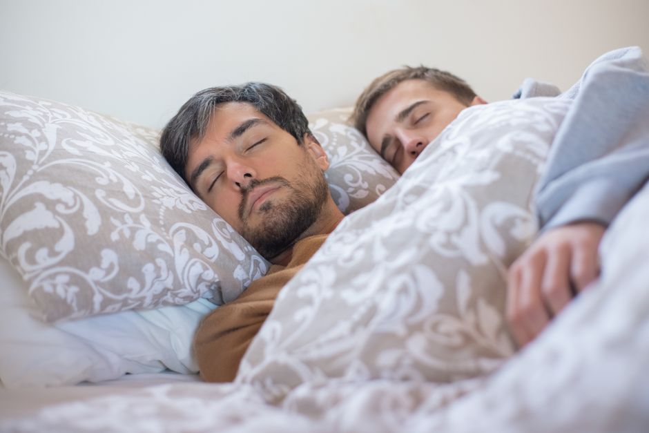 A loving couple peacefully sleeping together, embracing under a warm blanket indoors.