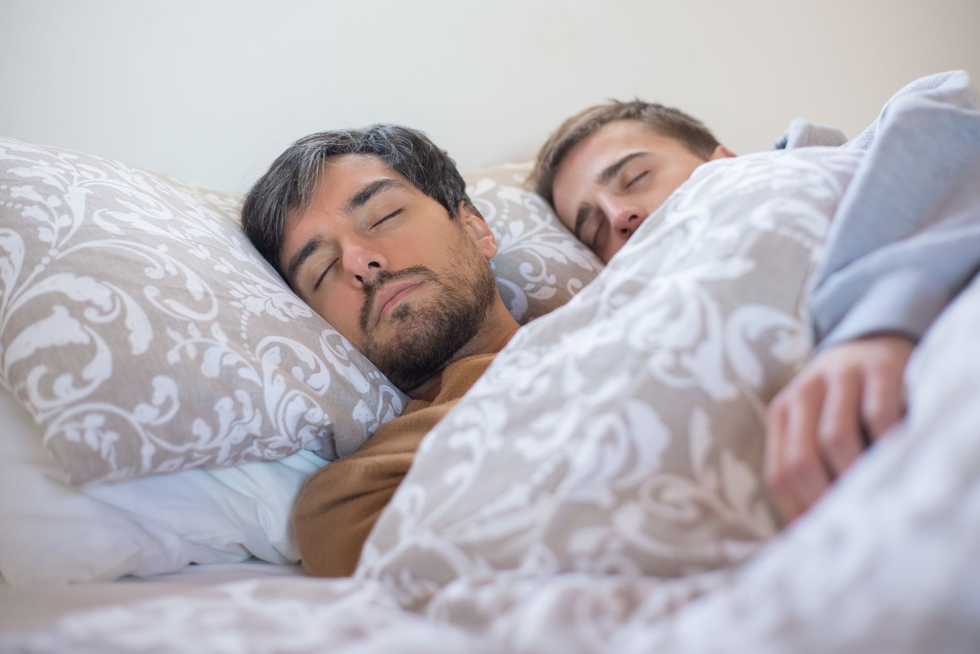 A loving couple peacefully sleeping together, embracing under a warm blanket indoors.
