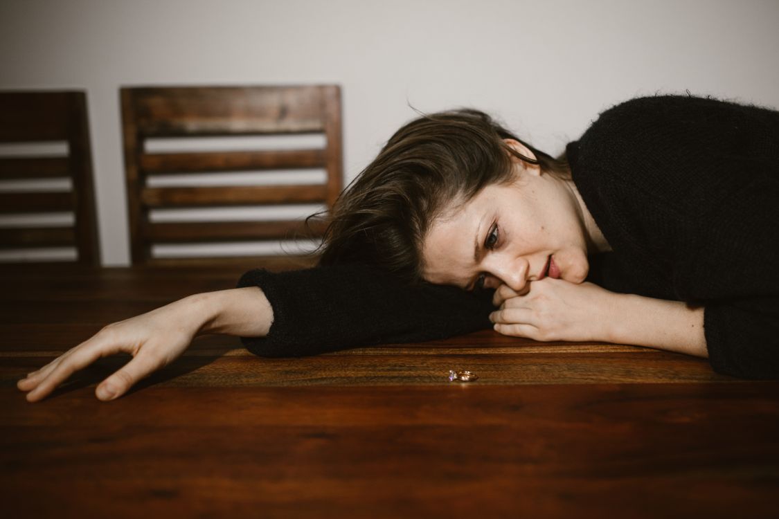 Free A woman lying on a wooden table, reflecting on a wedding ring, portraying emotions of sadness and contemplation. Stock Photo