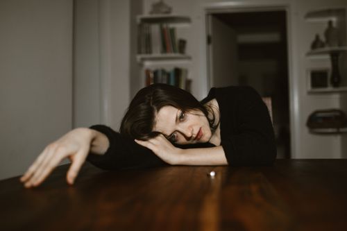 Free A thoughtful woman rests her head on a table in a dimly lit room, conveying a reflective mood. Stock Photo