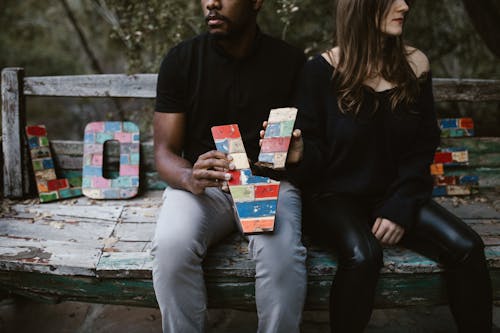 Free Man and Woman Sitting on Wooden Bench Holding a Broken Letter   Stock Photo