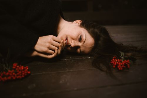 Free Caucasian woman on wooden floor surrounded by red berries, creating a moody composition. Stock Photo