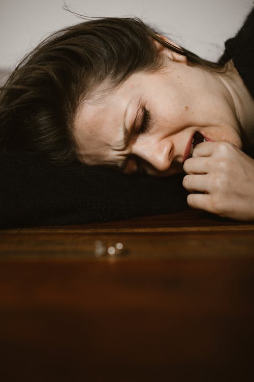 Free Sad Woman Biting Her Fingers While Lying Down on Wooden Surface  Stock Photo