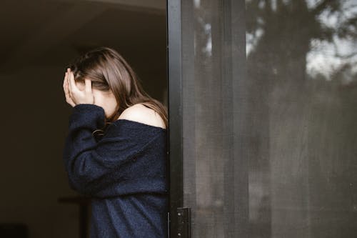 Woman Covering Her Face While Standing Near the Sliding Door 