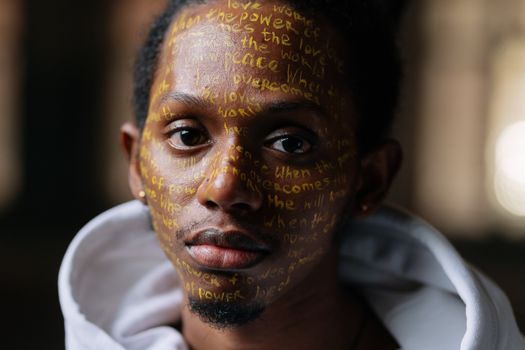 Close-up portrait of a man with inspirational messages written on his face, symbolizing peace and activism.