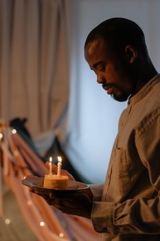 African American man holding a birthday cake with candles lit, celebrating indoors.