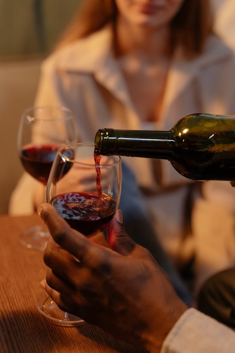 Selective Focus Photo Of A Person's Hand Pouring Wine Into A Glass