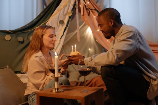 A couple celebrating a birthday indoors with candles and wine, creating a romantic atmosphere.