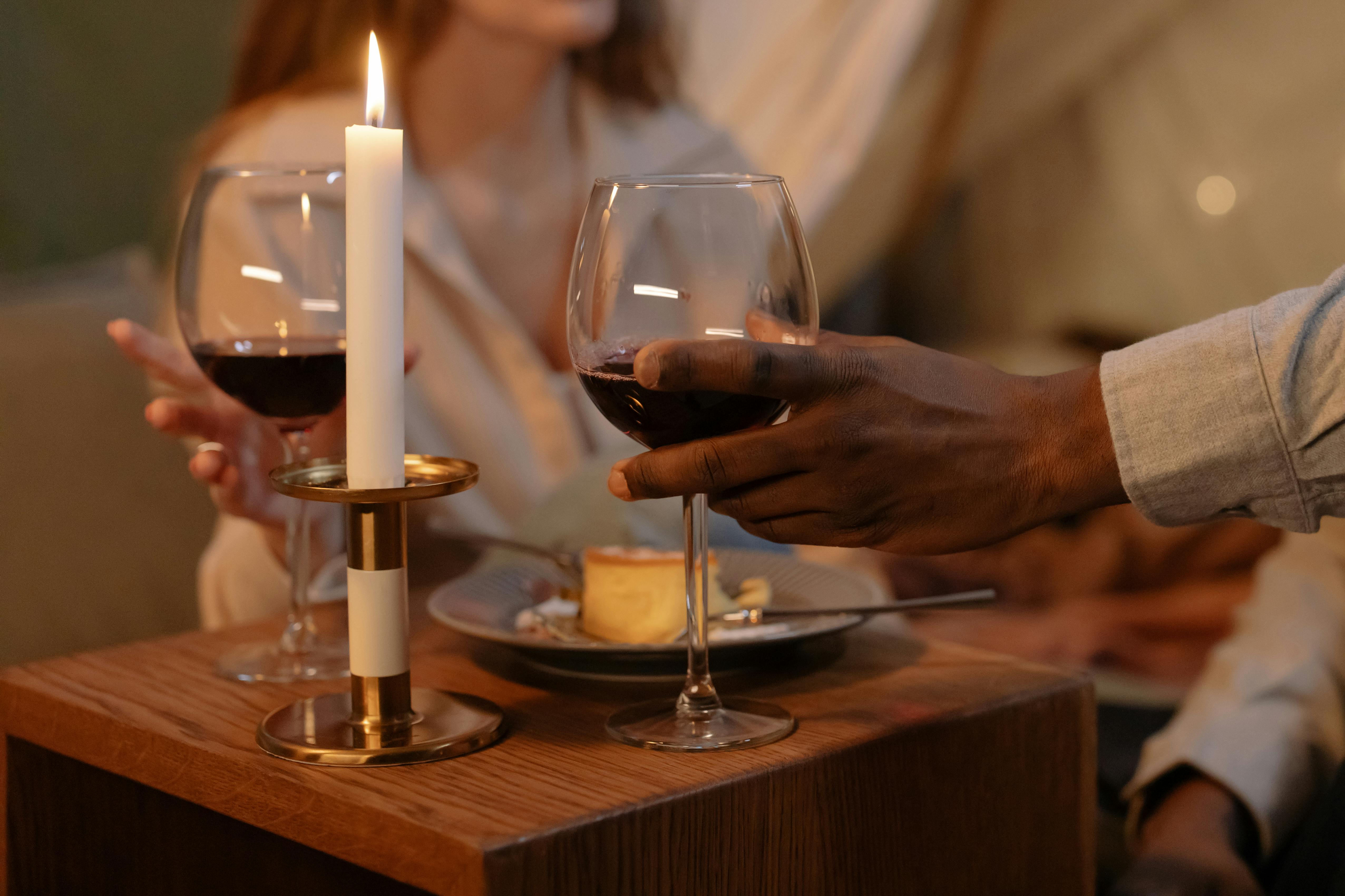 An intimate candlelit dinner setting with hands holding glasses of red wine, creating a warm ambiance.