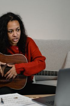 African American woman with guitar participating in an online music session from home