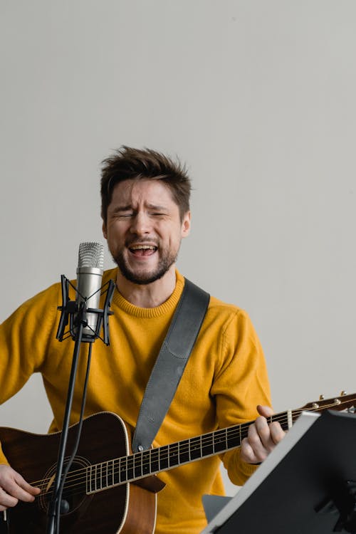 Man in a Yellow Sweater Playing a Guitar while Singing