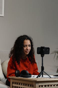 Woman with curly hair streaming online using a phone and headset at home.