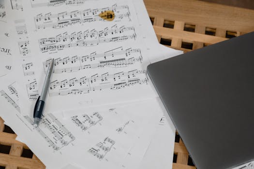 Close-up shot of music composition with laptop and guitar pick on a wooden table.