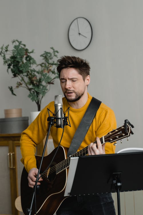 Photo of a Man Singing while Playing an Acoustic Guitar