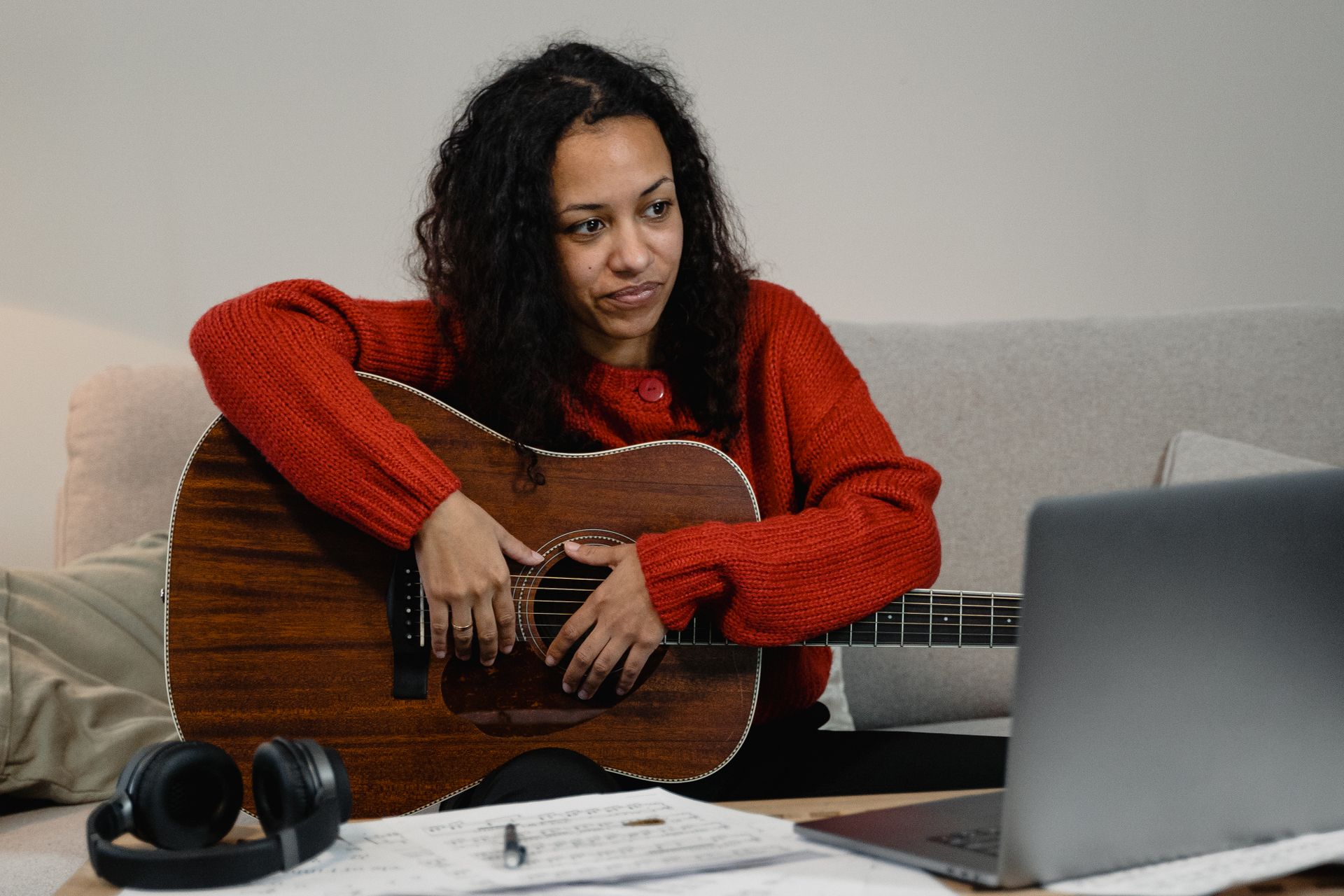 African American woman with guitar attends online music class from cozy home setting.