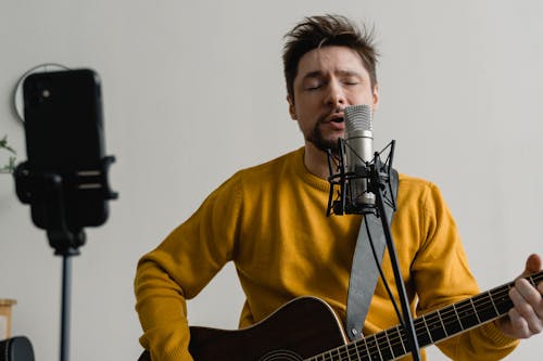 Free Photo of a Man in a Yellow Sweater Singing while His Eyes are Closed Stock Photo
