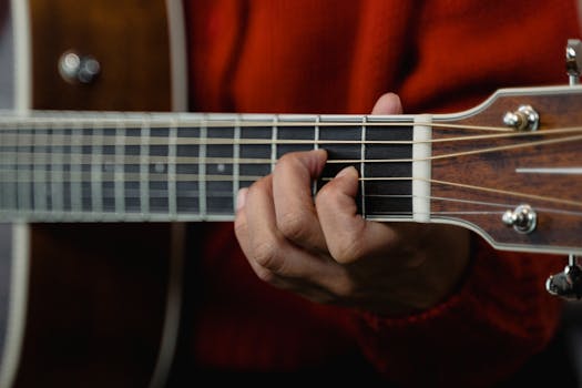 Detailed view of a hand playing a chord on an acoustic guitar, showcasing the fretboard and strings.