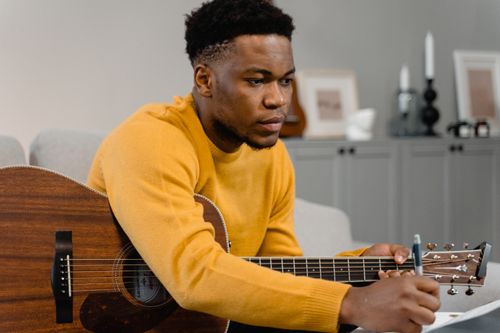 Free Musician playing acoustic guitar while writing notes in a cozy indoor setting. Stock Photo