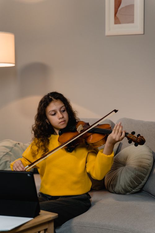 Free A young woman in a yellow sweater practices violin indoors, capturing the essence of musical dedication. Stock Photo