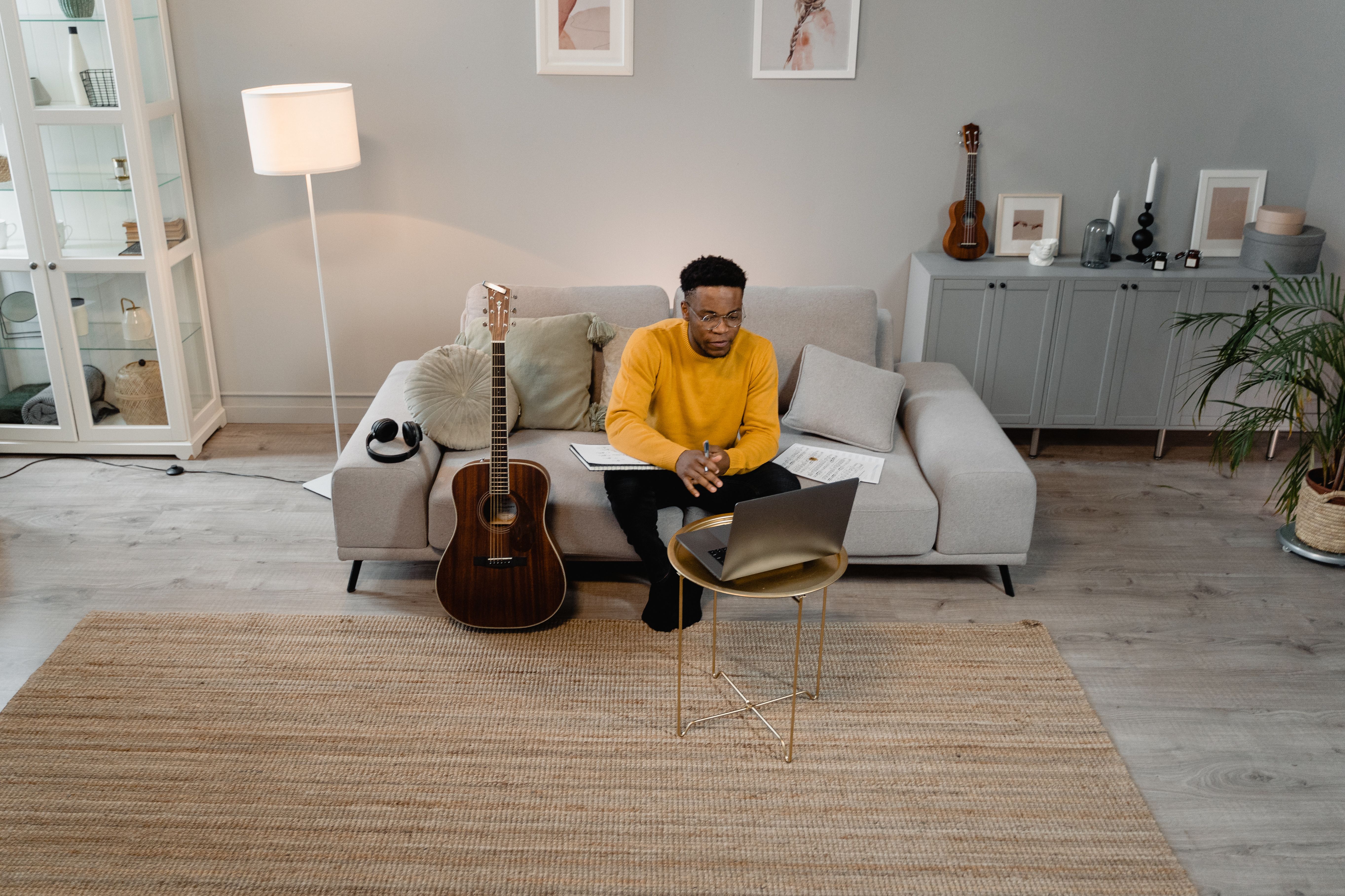 A man sits on a sofa with a laptop and guitar, creating a relaxed ambiance in a modern living room.