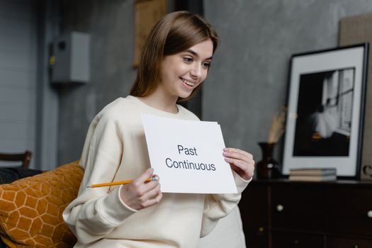 Caucasian woman teaching English grammar with a card indoors, holding a pencil and smiling.