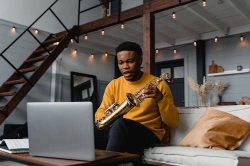Man Holding a Saxophone While Sitting In Front of a Laptop 