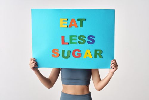 Free Woman holding colorful 'Eat Less Sugar' sign on white background promoting health awareness. Stock Photo