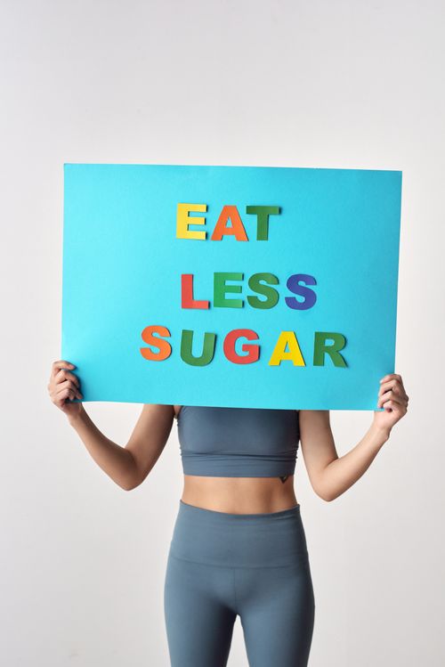 Free Woman in activewear holding a vibrant poster promoting less sugar intake. Stock Photo