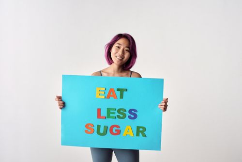 Free Asian woman with purple hair holding a colorful healthy eating poster saying 'Eat Less Sugar'. Stock Photo