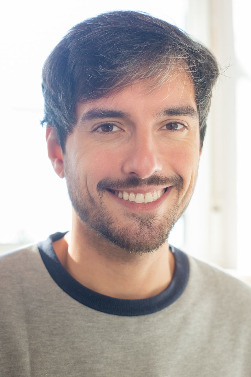 Portrait of a cheerful young man with a beard smiling indoors with natural light.