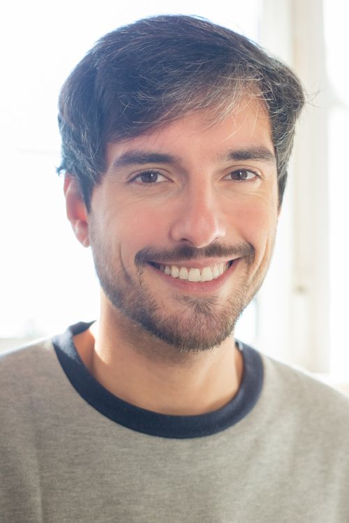 Free Portrait of a cheerful young man with a beard smiling indoors with natural light. Stock Photo